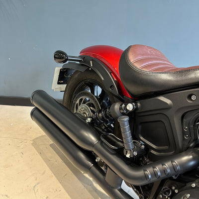 Red motorcycle with a brown seat against a gray wall.