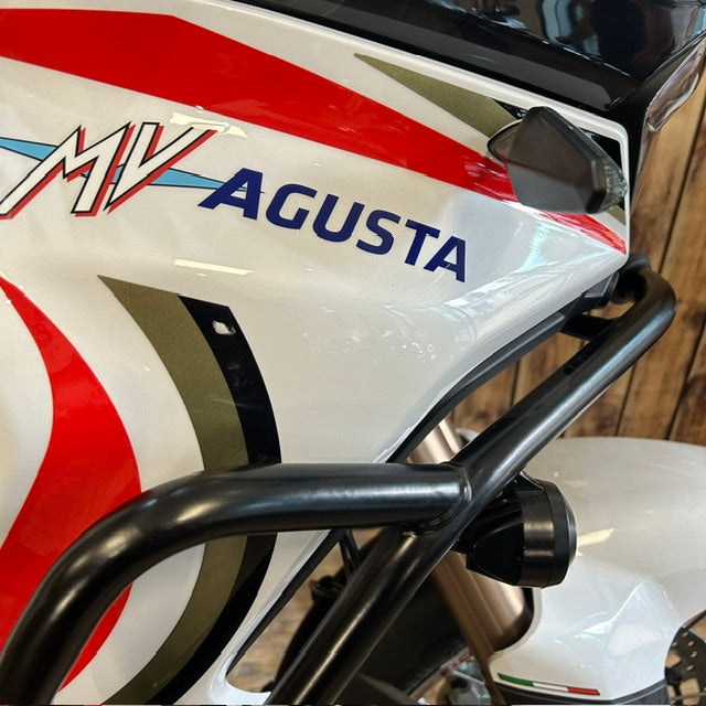Close-up of a white MV Agusta motorcycle body panel with red and olive graphic stripes, blue 'AGUSTA' lettering, and a black front protective bar.