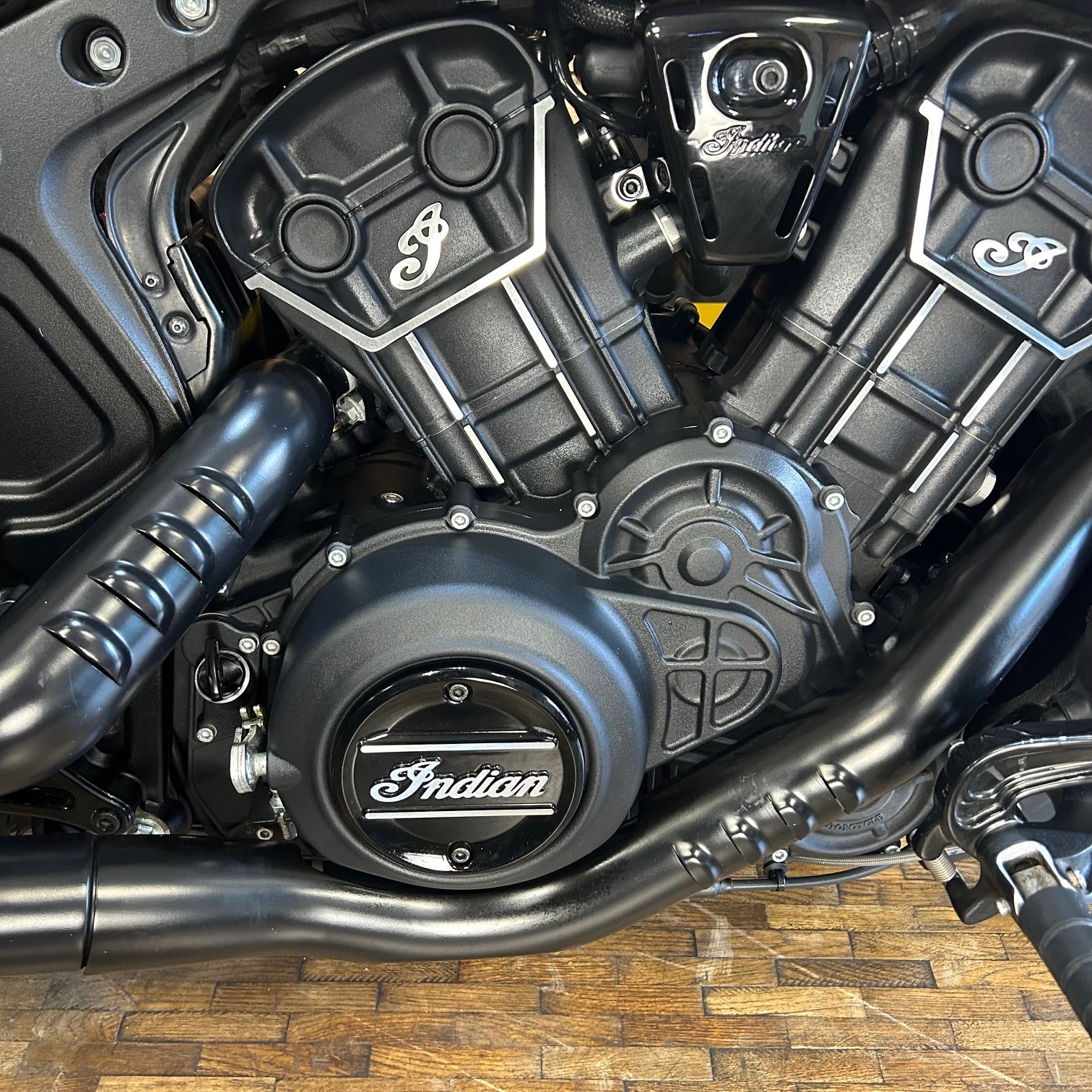 Close-up of a motorcycle engine with 'Indian' branding on a wooden floor.