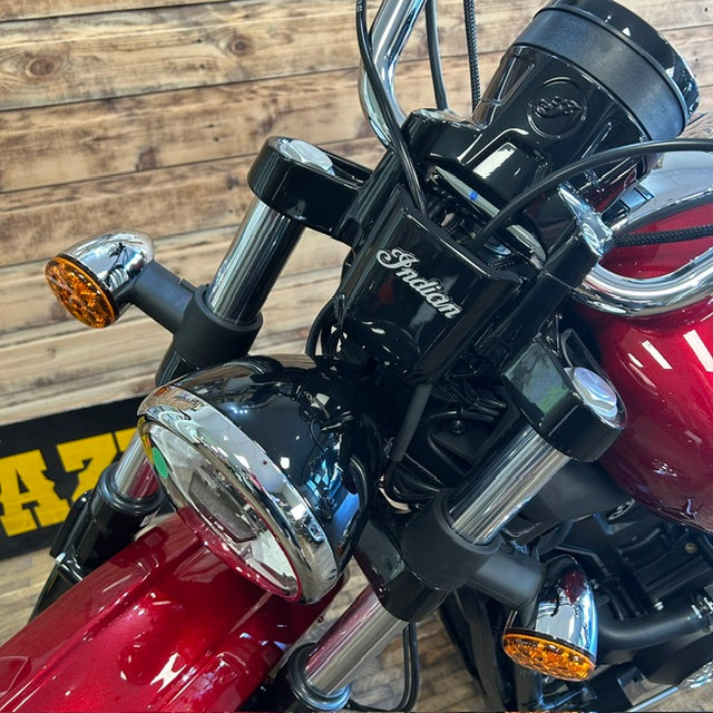 Close-up of the front of a red and black Indian motorcycle with chrome details, set against a rustic wooden plank wall.