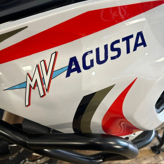 Close-up of a white motorcycle body panel with red, blue, black, and olive graphic decals, including the visible text 'MV AGUSTA'.