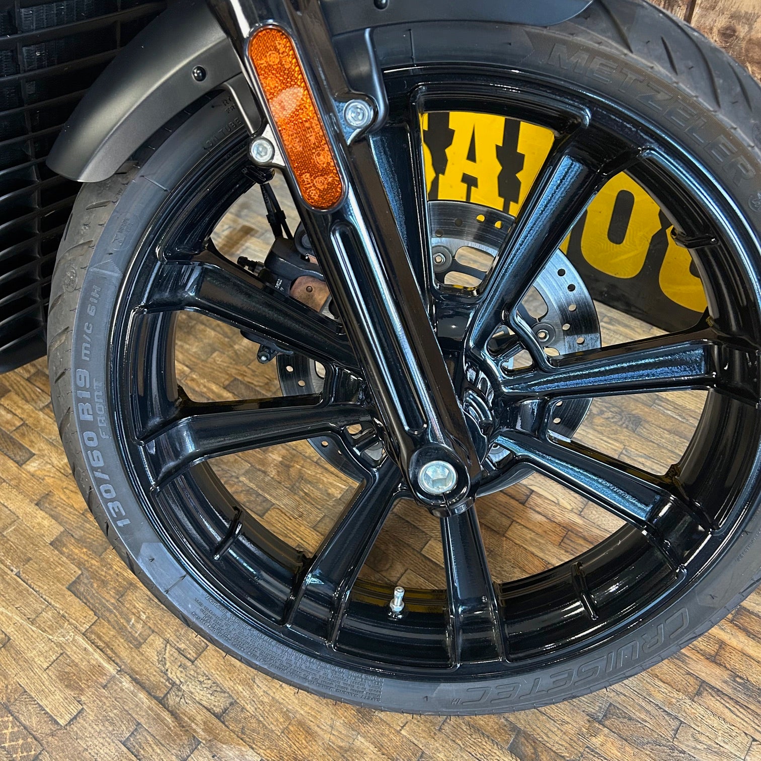 Close-up of a motorcycle wheel with a visible brand logo on a wooden floor.