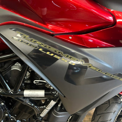 Close-up of a red and dark gray Yamaha Turismo Veloss 600 Lushi motorcycle body panel with gold lettering, showing the side fairing and engine components.