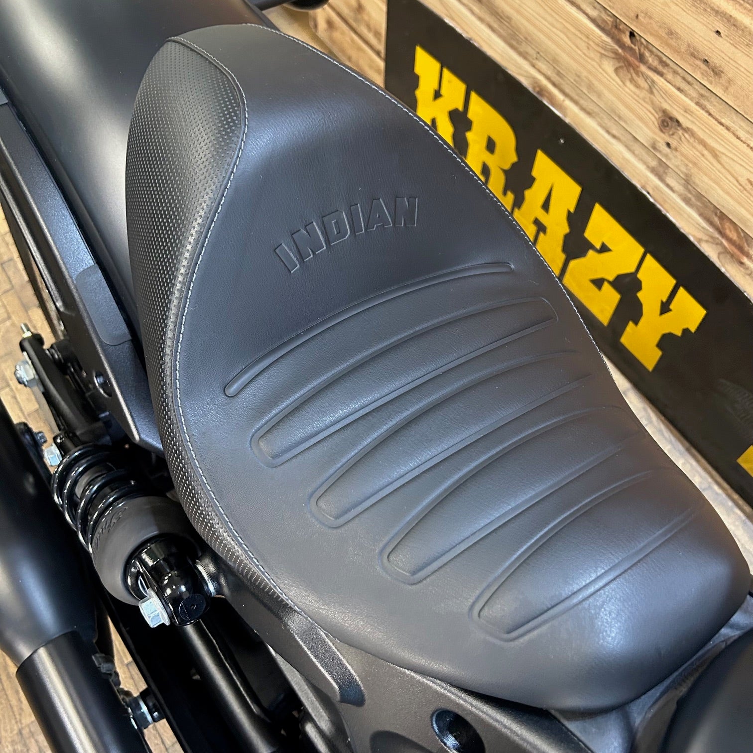 Gray motorcycle seat with 'Indian' branding on a wooden surface.