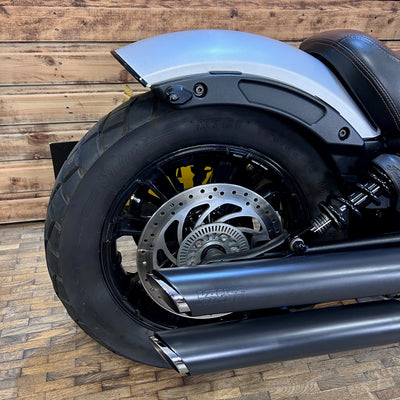 Close-up of a motorcycle's rear wheel and exhaust system on a wooden floor.